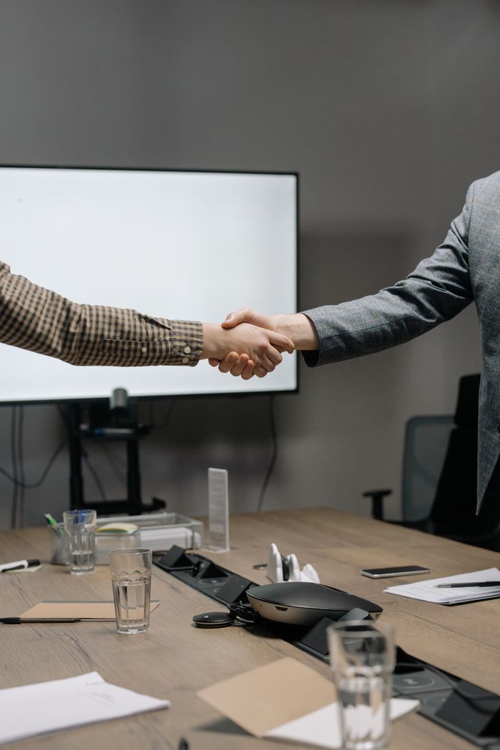 services-04 Two business professionals shaking hands in a modern meeting room, symbolizing successful collaboration.
